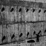 Dois trabalhadores pintam uma grande parede de concreto em um ambiente industrial.