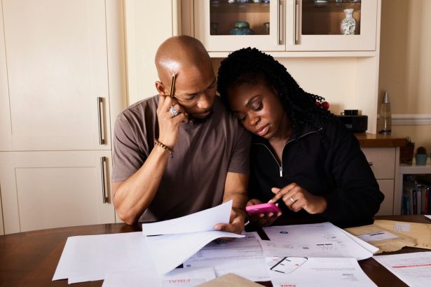 Casal organiza as finanças domésticas à mesa, analisando documentos e usando um smartphone.