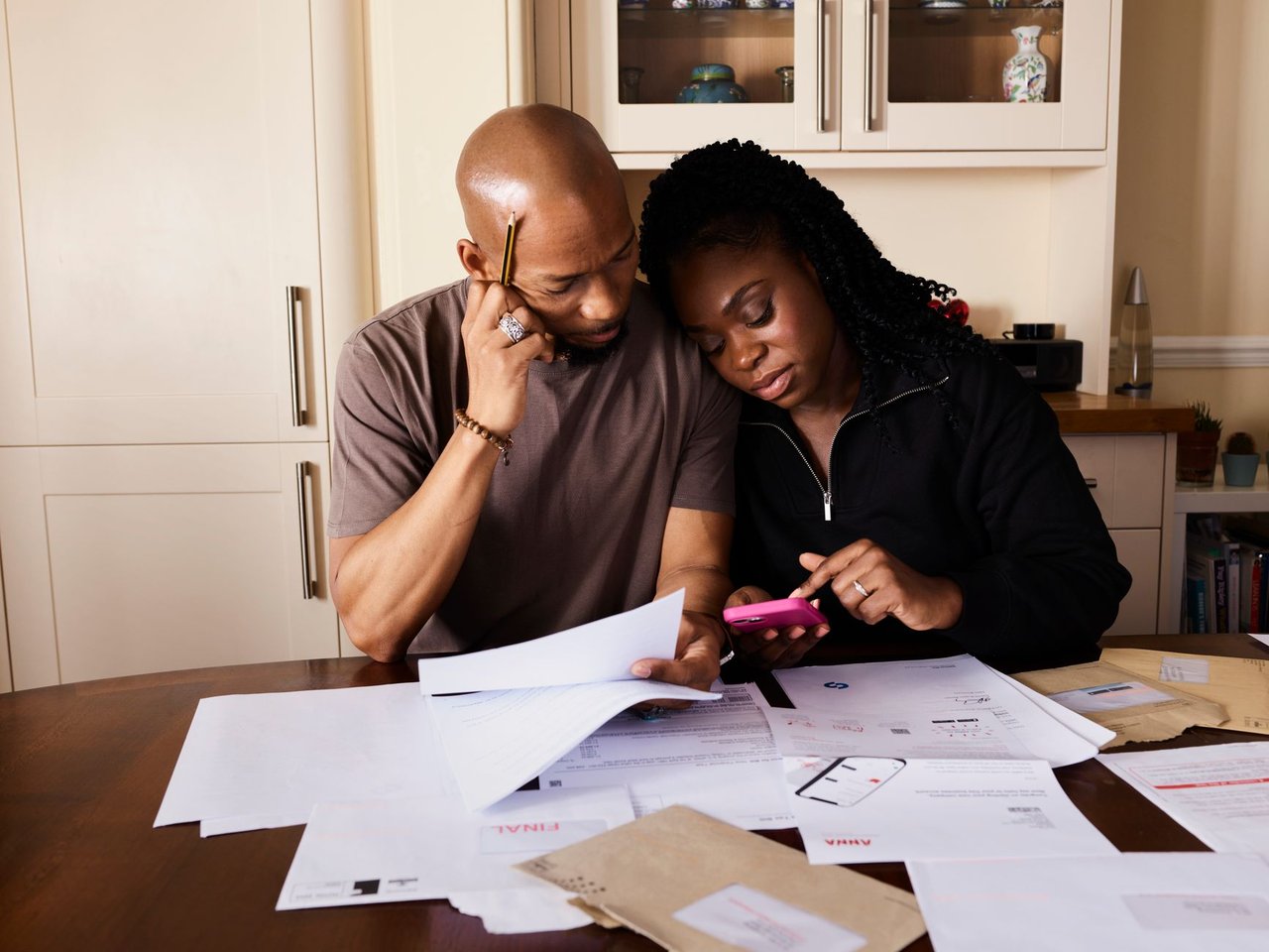 Casal organiza as finanças domésticas à mesa, analisando documentos e usando um smartphone.