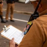 Policial registra informações em uma prancheta ao ar livre.