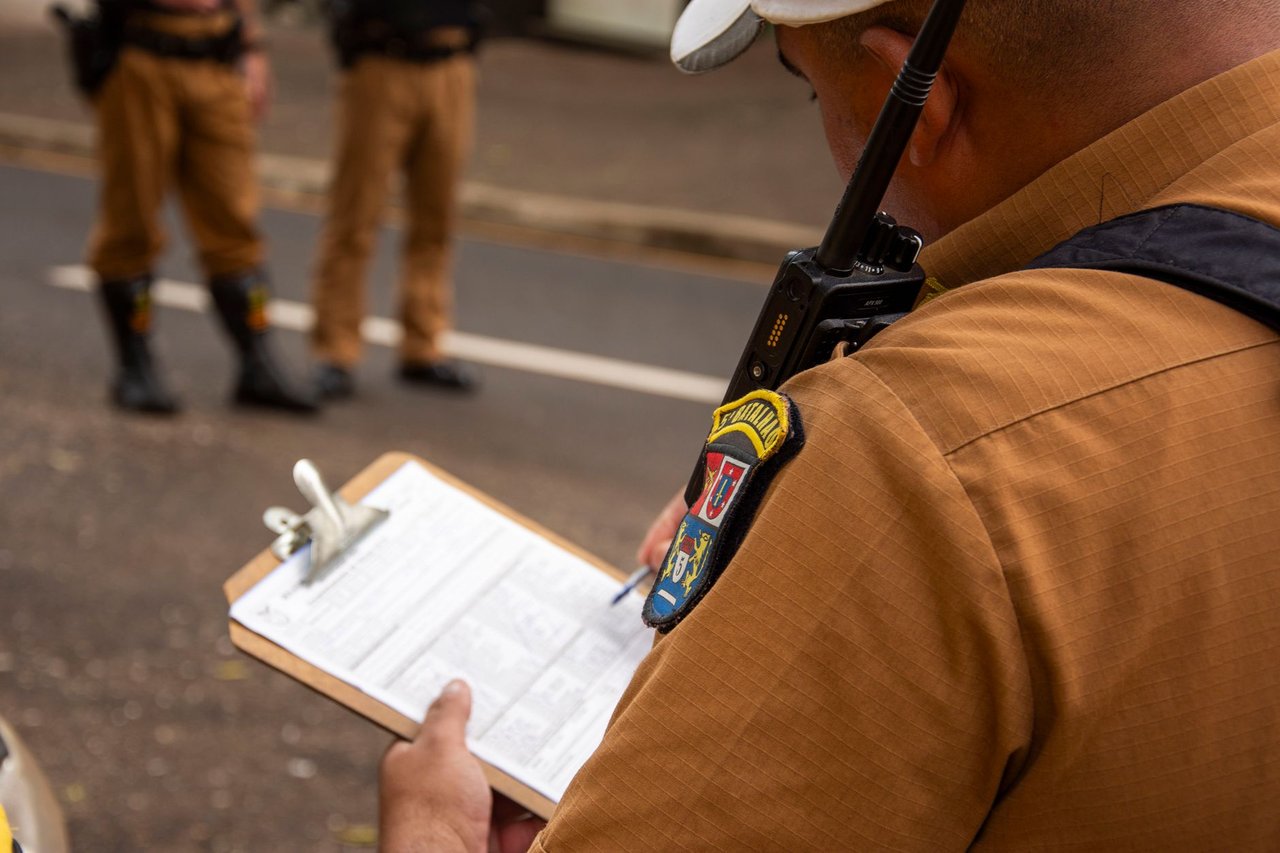 Policial registra informações em uma prancheta ao ar livre.