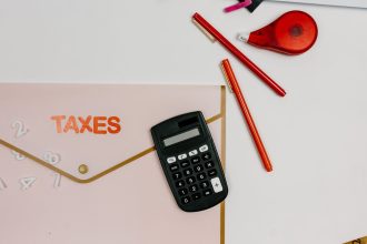 Calculadora, canetas e pasta com a inscrição “TAXES” sobre uma mesa de escritório.
