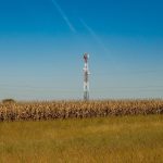 Torre de comunicação instalada em um campo rural, sob céu azul.