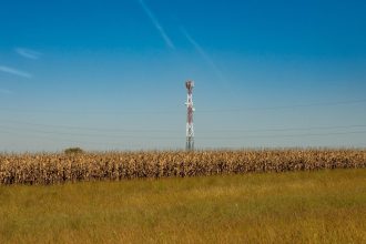 Torre de comunicação instalada em um campo rural, sob céu azul.