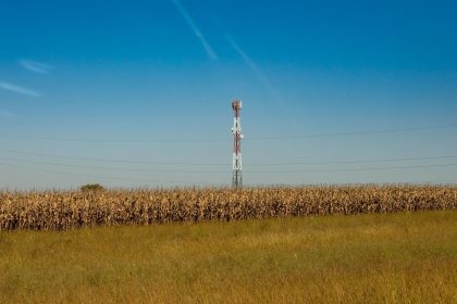 Torre de comunicação instalada em um campo rural, sob céu azul.