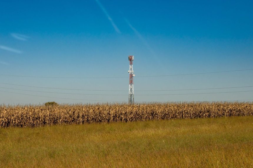 Torre de comunicação instalada em um campo rural, sob céu azul.