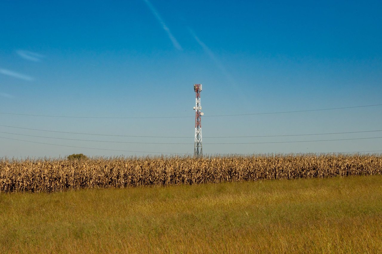 Torre de comunicação instalada em um campo rural, sob céu azul.
