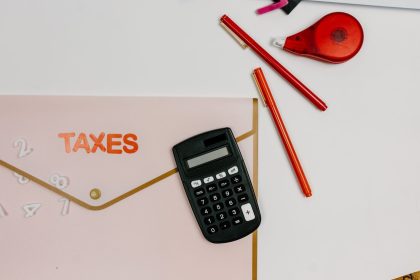 Calculadora, canetas e pasta com a inscrição “TAXES” sobre uma mesa de escritório.