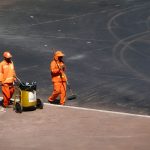 Dois trabalhadores da limpeza urbana atuam em uma rua de Brasília, usando uniformes laranja.