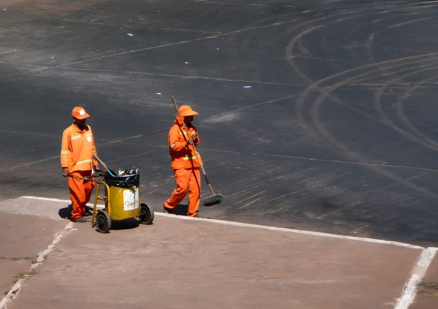 Dois trabalhadores da limpeza urbana atuam em uma rua de Brasília, usando uniformes laranja.