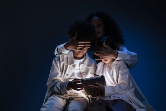 Mãe acompanha duas crianças durante o uso de um tablet, em contexto de supervisão e segurança digital.