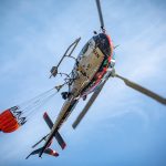 Helicóptero equipado com bolsa de água sobrevoa uma área de floresta atingida por incêndio florestal